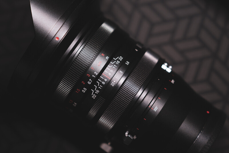 Close-up of a vintage manual focus lens with aperture and focus rings visible against dark fabric.