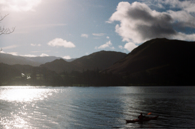 A small boat on a lake with forested mountains under a partly cloudy sky.