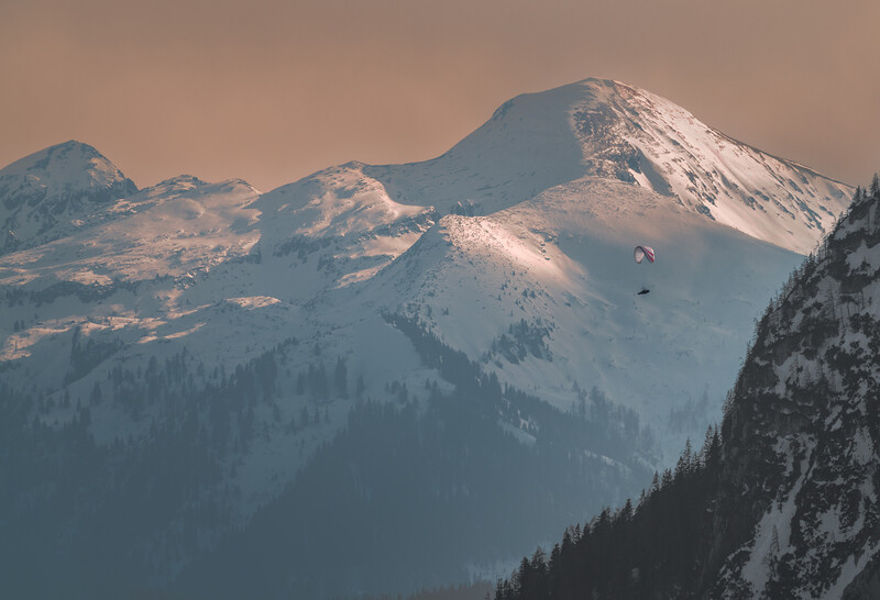 Snow-covered mountain peaks with forested slopes under warm, hazy light.
