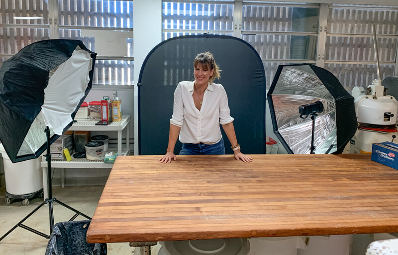 Woman posing at wooden table during professional portrait photography setup with studio lighting.