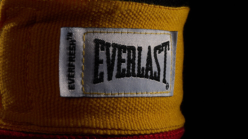 Close-up of yellow and red boxing hand wraps with Everlast brand label visible against dark background.
