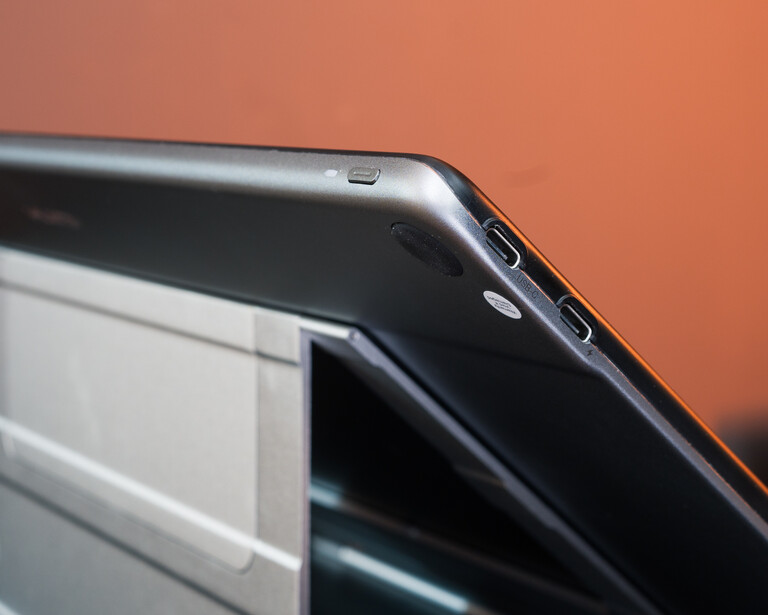Close-up of a tablet device's top edge showing ports and curved bezel against warm orange background.