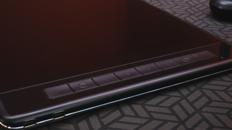 Close-up of a laptop's edge showing control buttons and metallic trim against a patterned surface.