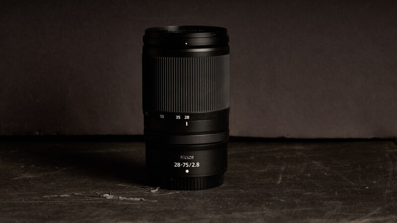 Sony 28-75mm f/2.8 lens positioned vertically on a dark textured surface.