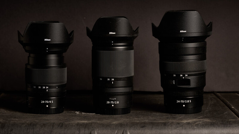 Three Nikon Z-mount lenses with lens hoods displayed side by side on a wooden surface against a dark background.