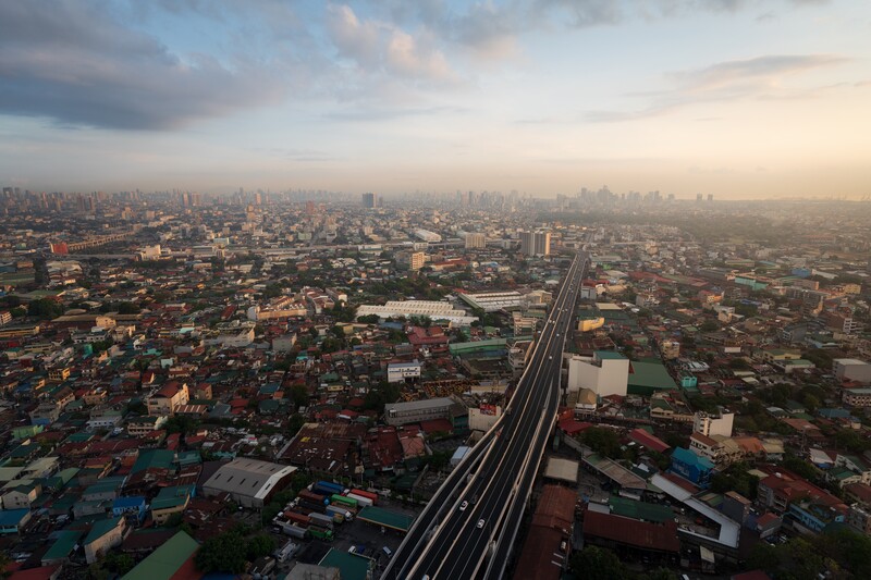 Elevated highway cutting through a dense urban sprawl at dusk with hazy skyline.