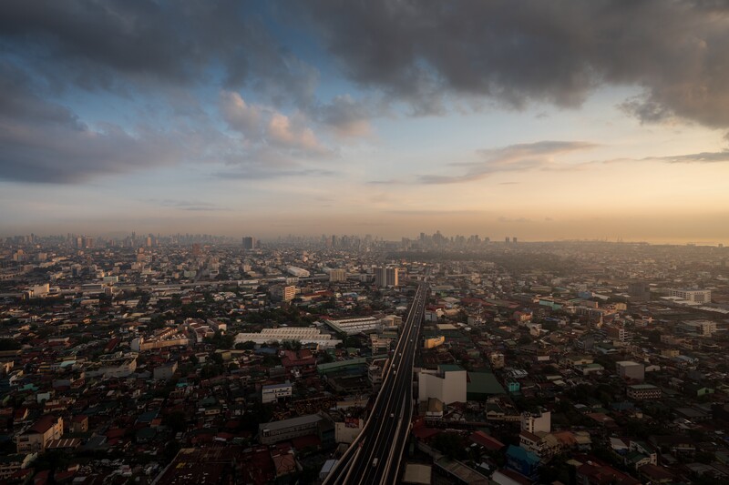 Aerial view of a sprawling cityscape at dusk with a highway cutting through dense urban development beneath dramatic clouds.