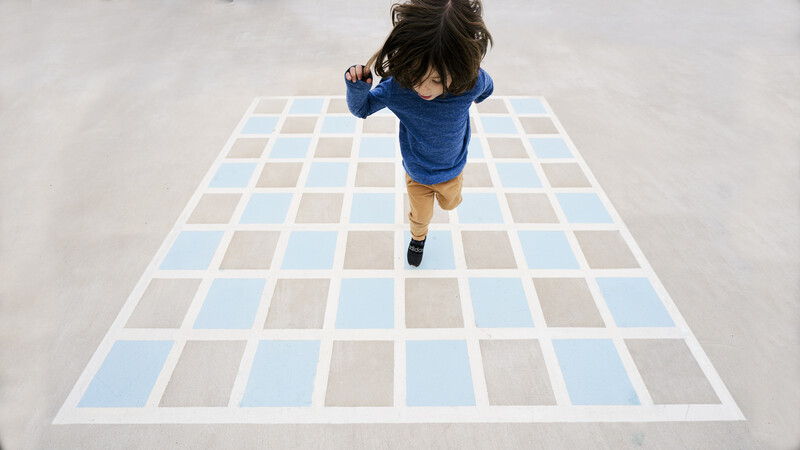 Overhead view of a child running on a checkered floor pattern in blue and gray tiles.