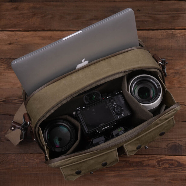 Canvas camera bag open on wooden surface displaying organized camera gear and laptop.