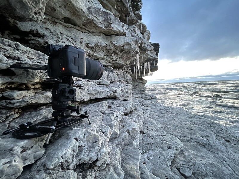 Camera mounted on rocky cliff face overlooking expansive valley landscape.