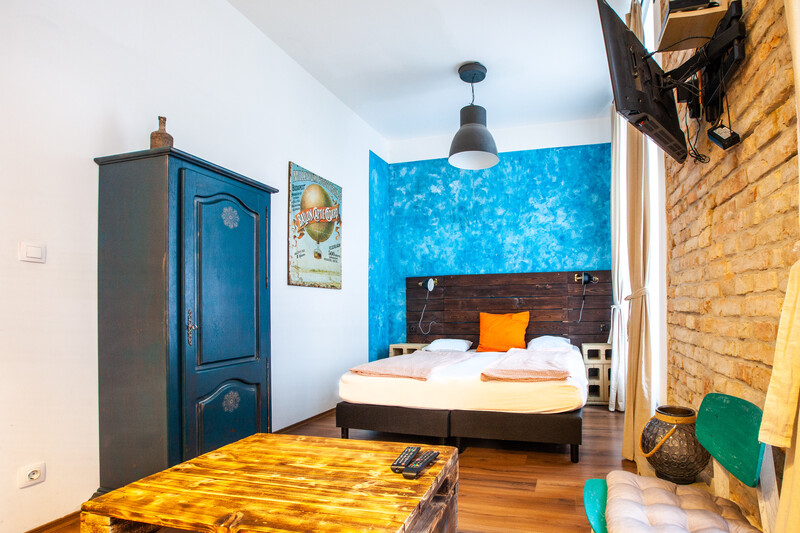 Bedroom interior with bright blue accent wall, wooden bed frame, and contrasting yellow furniture piece in foreground.