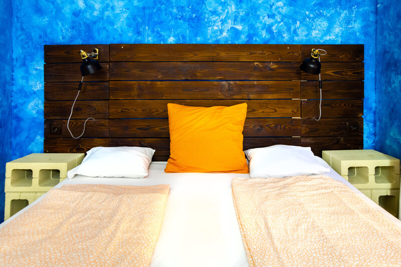 Modern bedroom with dark wood headboard, blue textured wall, and bright orange accent pillow centered on white bedding.