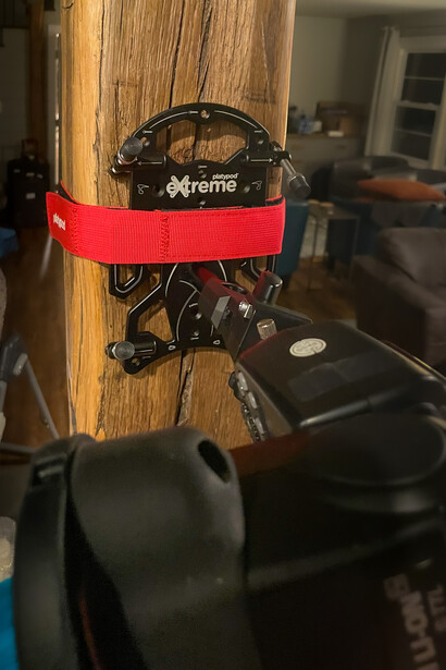 Camera gear mounted on wooden wall with red strap and black equipment below.