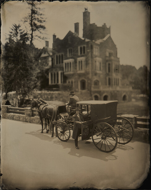 Horse-drawn carriage parked on a tree-lined path with a large Victorian mansion in the background.