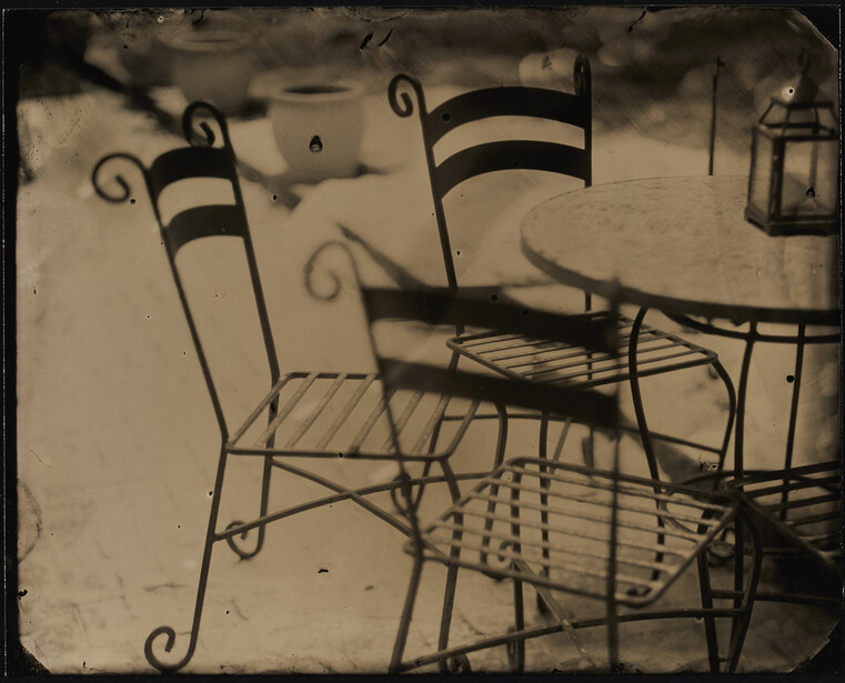 Ornate iron chairs with striped fabric casting long shadows on a textured surface.