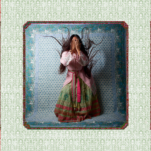 Woman with fairy wings lying face-down on patterned fabric, wearing a colorful skirt with red sash.