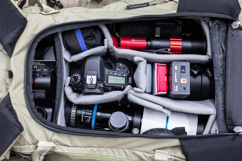 Photography gear organized in a canvas camera bag with multiple lenses, flashes, and accessories neatly arranged in padded compartments.