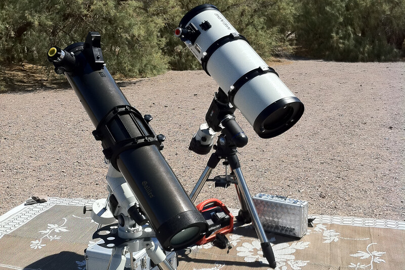 Two refractor telescopes mounted on tripods outdoors, with one black and one white tube angled toward the sky.