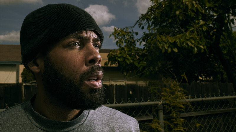 Bearded man in black beanie looking upward with an expression of wonder or contemplation.