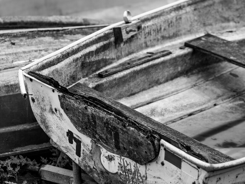 Weathered wooden boats stacked and abandoned, shot in black and white with shallow depth of field.