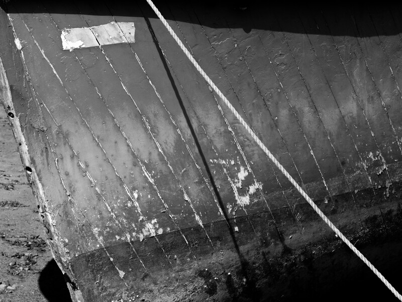 Close-up of weathered wooden boat hull showing rope rigging and peeling white paint against dark water.