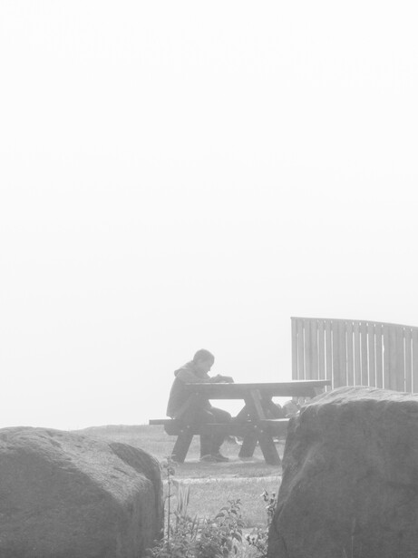 Person sitting on hay bales with wooden fence structure in background, shot in black and white.