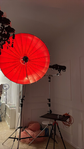 Studio lighting setup with red umbrella reflector and tripod-mounted monolight against gray wall.