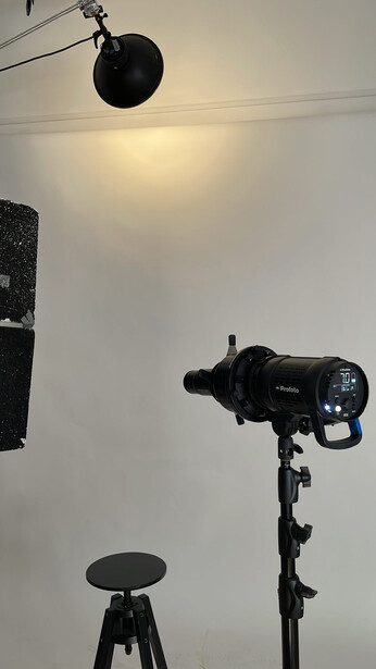 Studio lighting setup with mounted monolight on tripod and reflective light modifier suspended overhead.