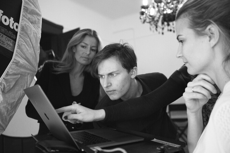 Three people gathered around a laptop reviewing work together in a black and white photograph.
