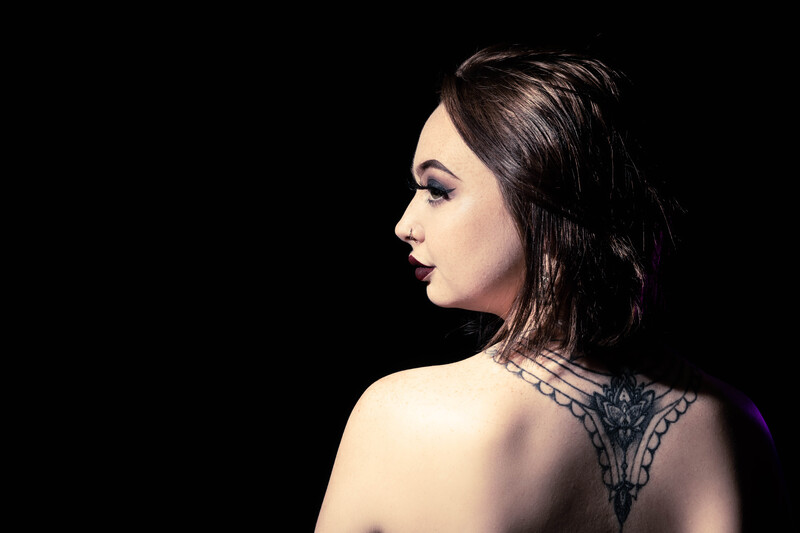 Woman in profile against black background with decorative back tattoo.