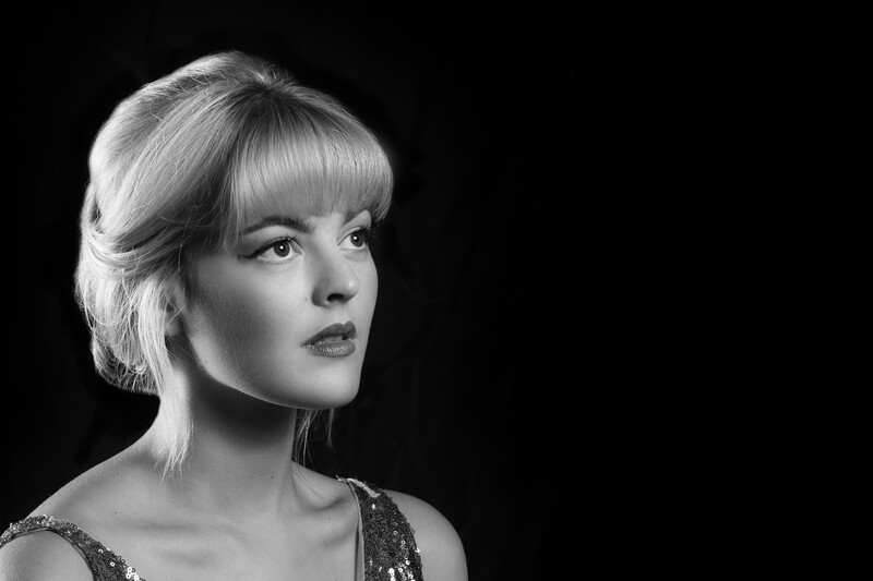 Woman in profile against black background, platinum blonde bob with bangs, dramatic side lighting.