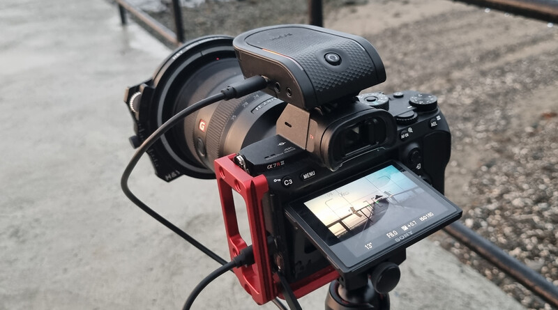 Sony mirrorless camera on red rig with monitor and wireless headphones mounted on tripod.