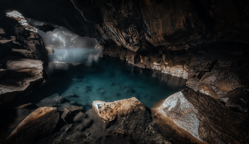 Underground cave pool with turquoise water surrounded by rocky limestone formations and dramatic natural lighting.