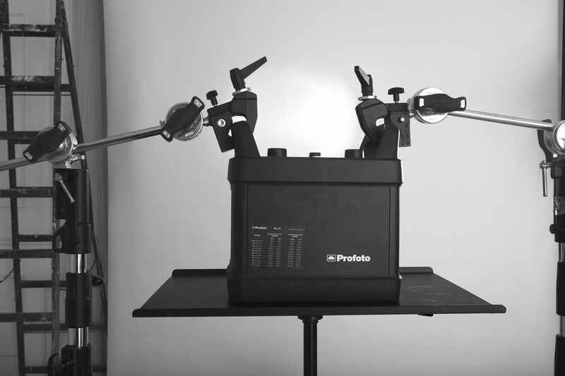 Professional studio lighting setup with Profoto power pack and dual articulating arms mounted on stand.