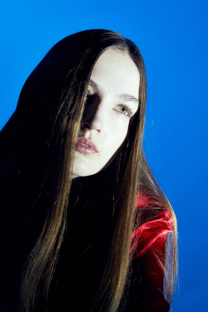 Woman with long dark hair wearing red velvet against solid blue background.