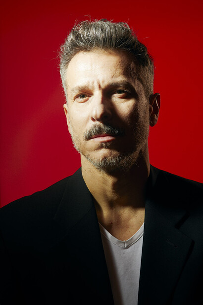 Male portrait against solid red background with studio lighting.