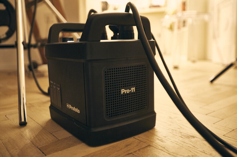 Profoto Pro-11 power pack with carrying handles sits on wooden floor in studio setting.