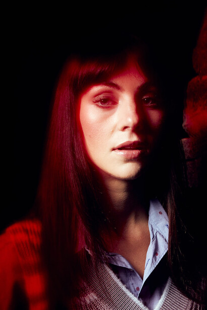 Woman with long straight hair lit by red light against dark background.