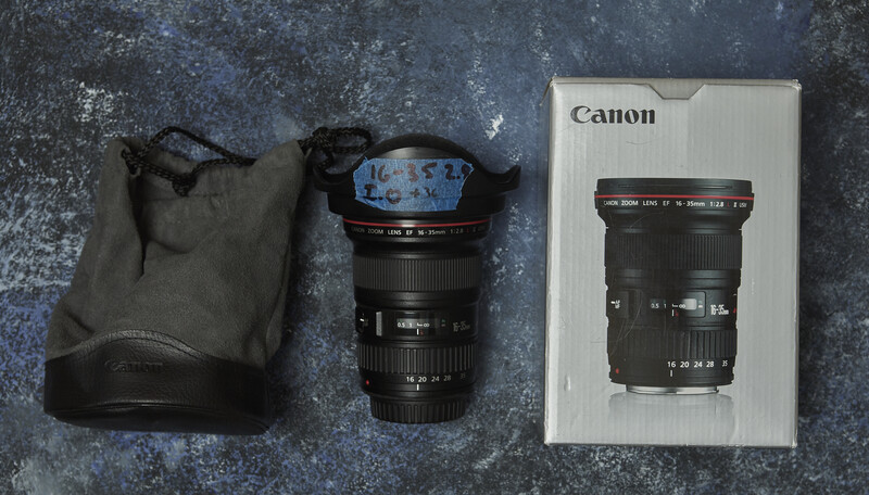Canon wide-angle zoom lens with protective pouch and instruction manual displayed on textured surface.