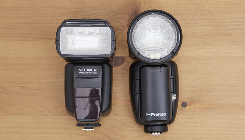Two external camera flashes positioned side by side on a wooden surface for comparison.