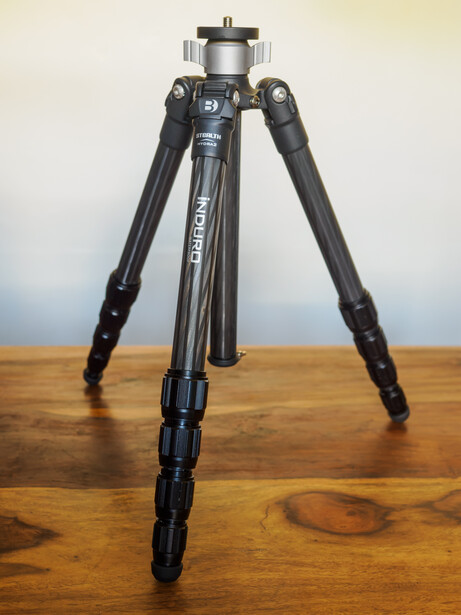 Professional carbon fiber tripod with extended legs and ball head mounted on wooden surface.
