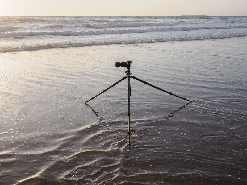 Camera mounted on a tripod standing in shallow ocean water with waves in the background.