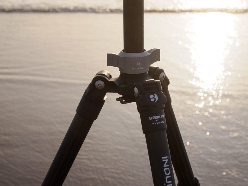 Tripod with legs extended against a backlit water landscape at golden hour.