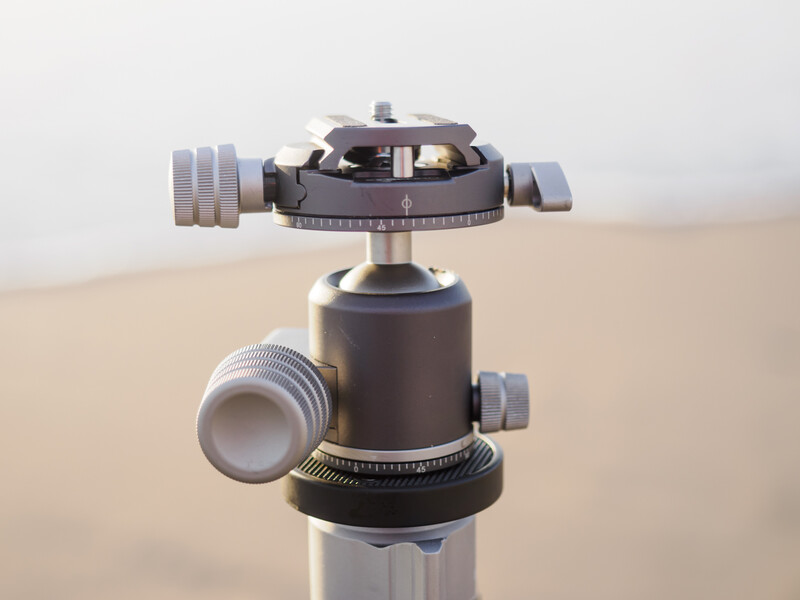 Ball head tripod mount with gray finish and adjustment knobs, photographed against a neutral beige background.