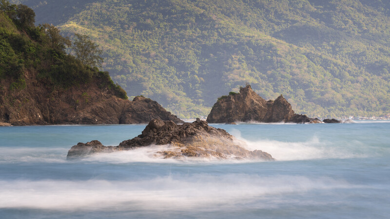 Rocky island formations surrounded by misty water with forested mountains in the background.