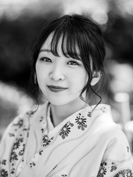 Woman in patterned white shirt with bangs, smiling softly at camera in black and white portrait.