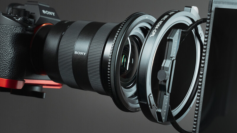 Sony camera lens with wide-angle converter and filter adapter attached, displayed against dark background.