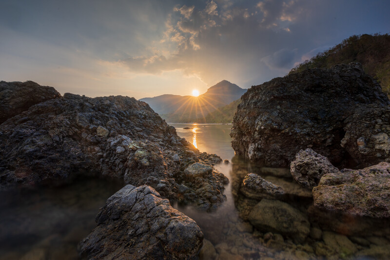 Sun rising between two rocky outcrops above a calm body of water at dawn.