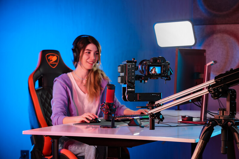 Content creator seated at desk with professional camera on gimbal and LED lighting setup.