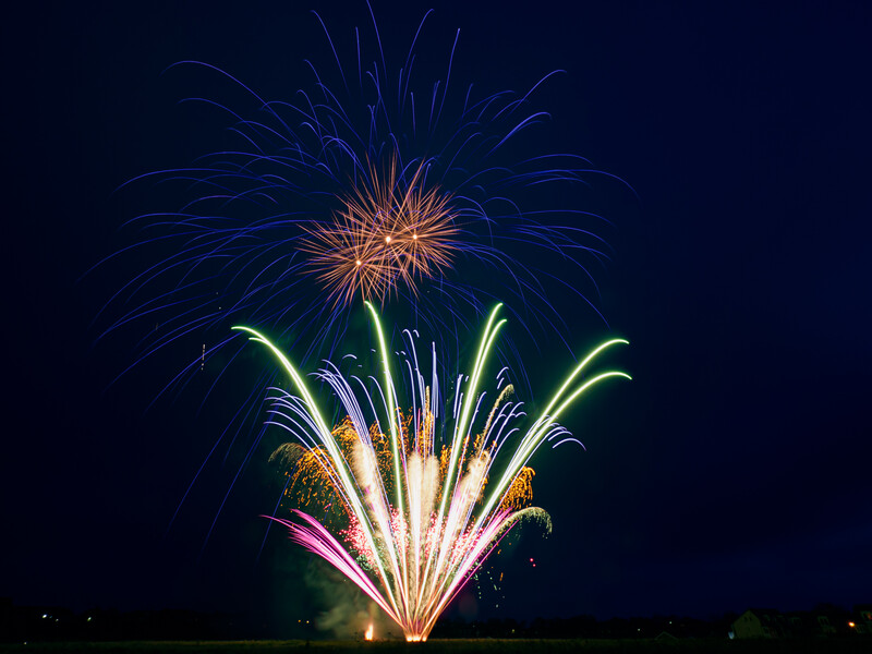 Fireworks bursting in the night sky with blue, green, pink, and gold sparks radiating outward.